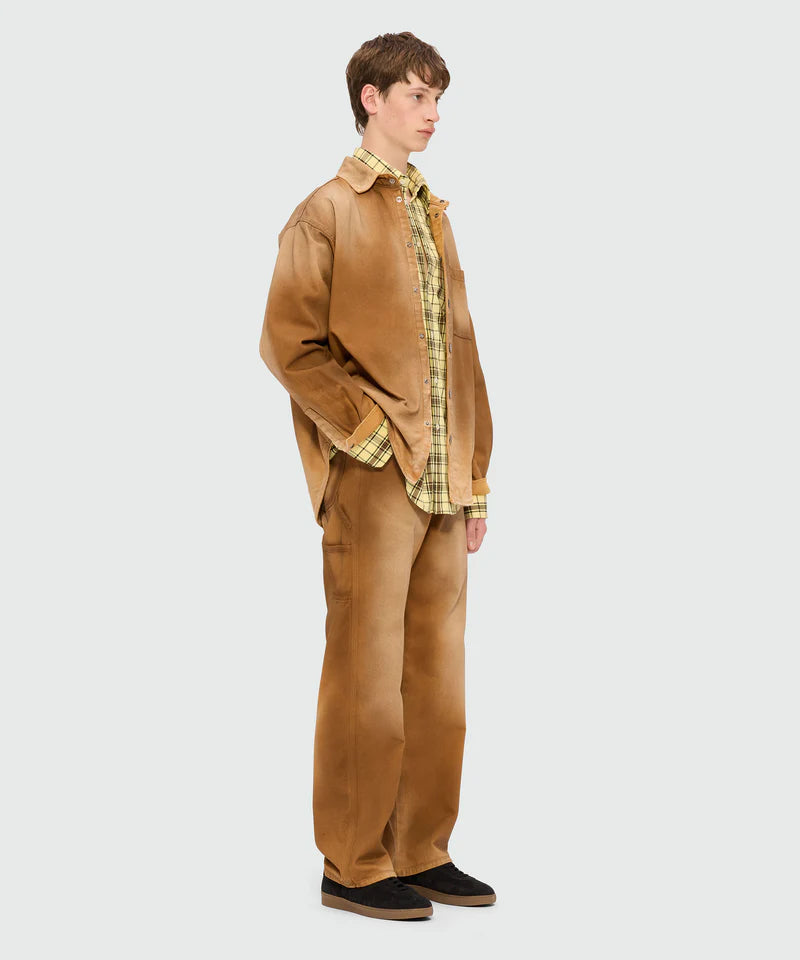 Model wearing a long-sleeved yellow viscose shirt with check pattern and oversized fit, paired with brown pants.
