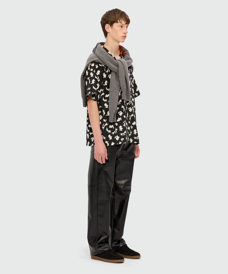 Model wearing a black poplin bowling shirt with 'Follow the Rabbit®' print and relaxed pants.