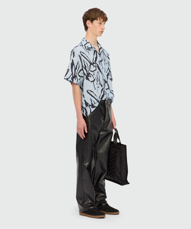 Side view of a model wearing a light blue striped poplin bowling shirt with 'Sketched Bunnies' print and black pants.