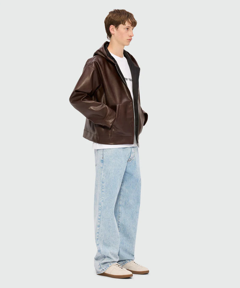 Model wearing a brown leather jacket over a white T-shirt and light blue jeans, showcasing a casual streetwear style.