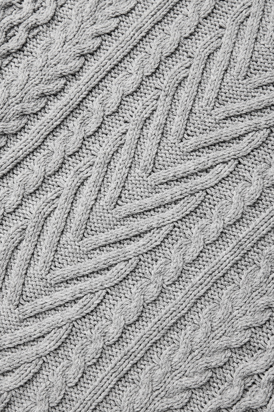 Close-up of a cable knit texture in a light gray color, showcasing chunky patterns of a crew neck sweater design.