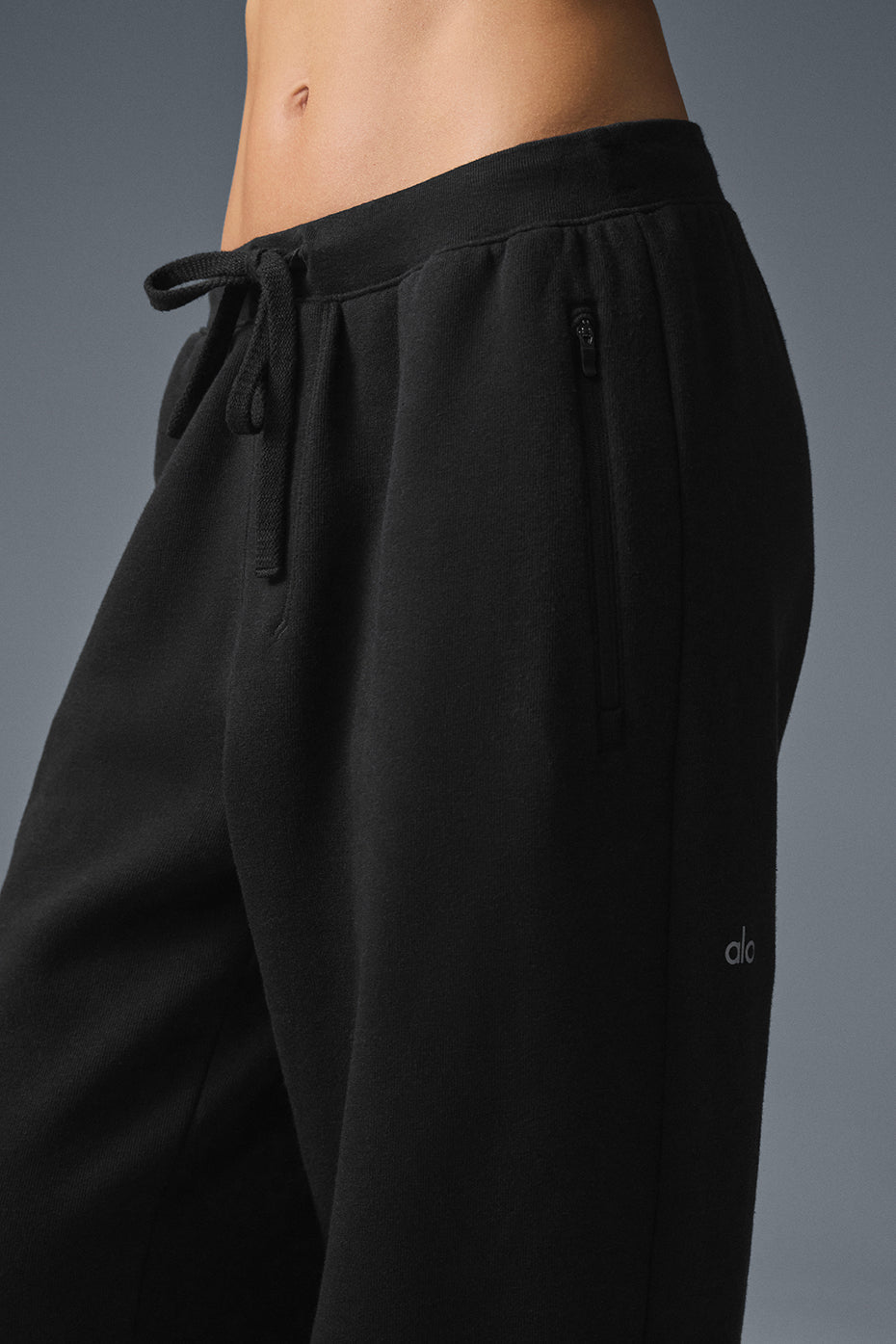 Close-up of black Triumph Restore Sweatpant featuring drawcord waistline and zippered pockets.