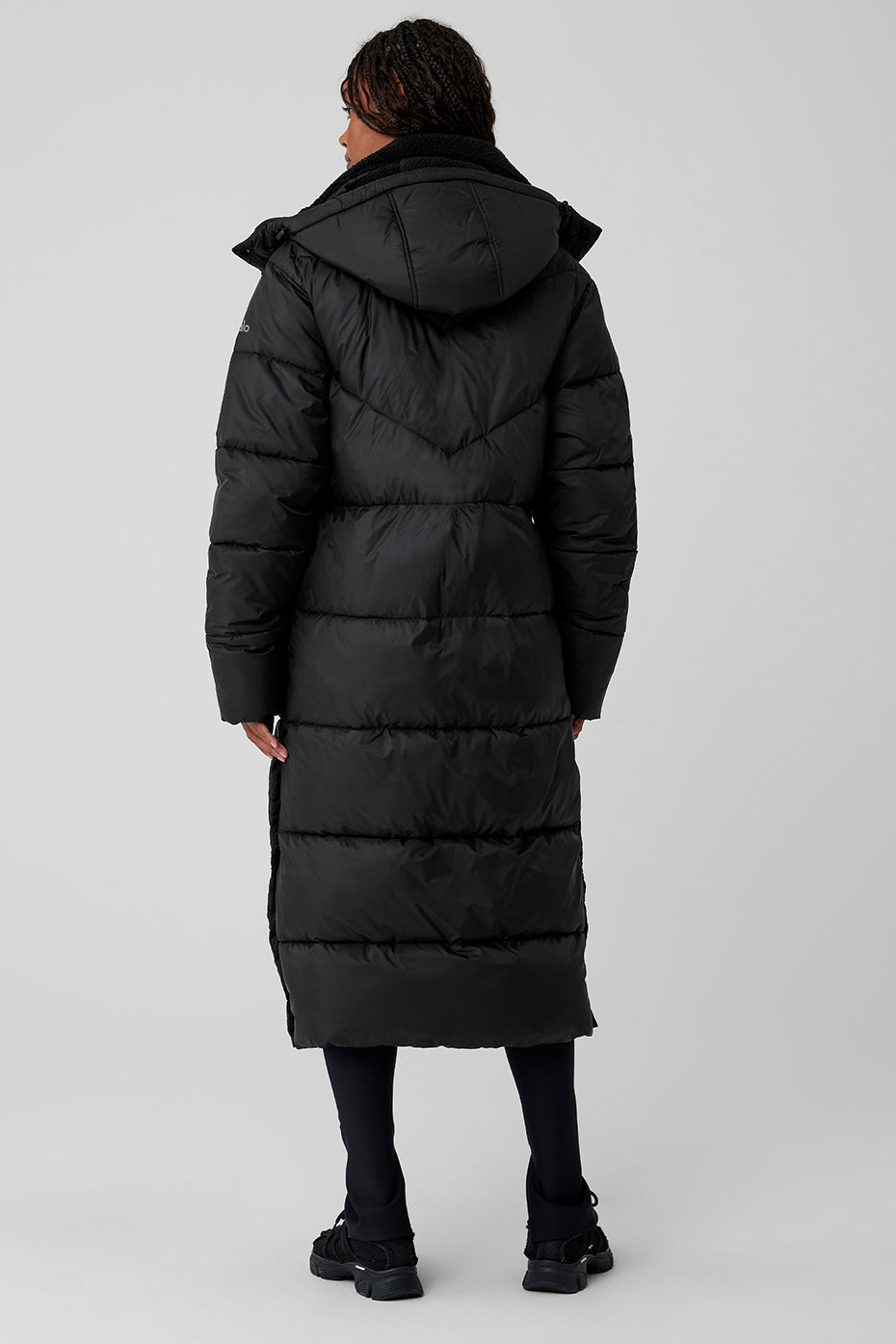 Back view of a woman wearing a long black Gold Rush Puffer Trench with a hood, ideal for winter warmth and style.