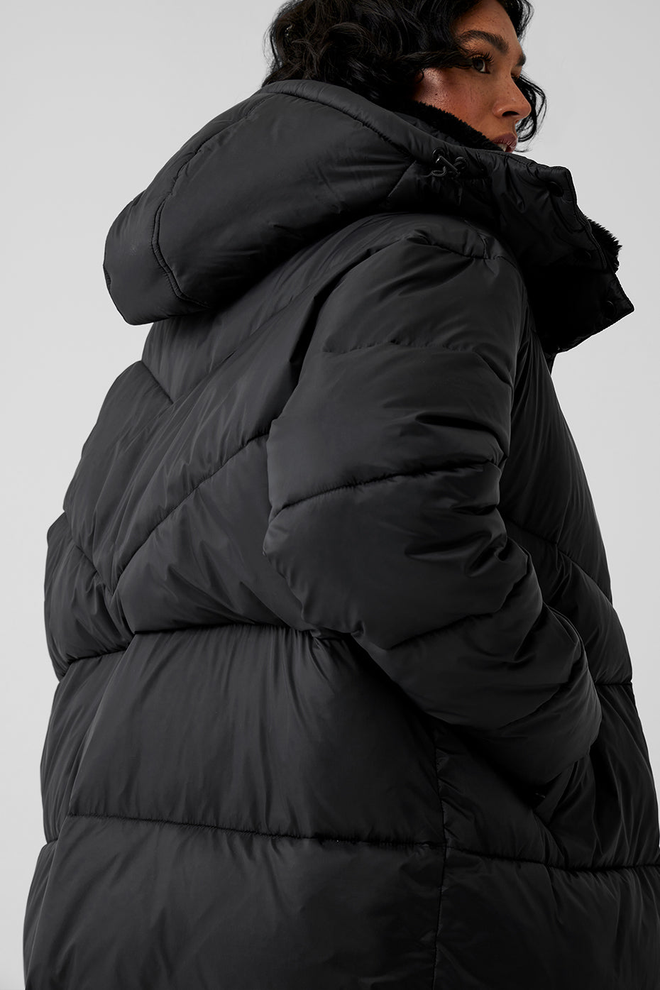 Model in oversized black puffer coat featuring a hood, showcasing winter outerwear style for chilly weather.