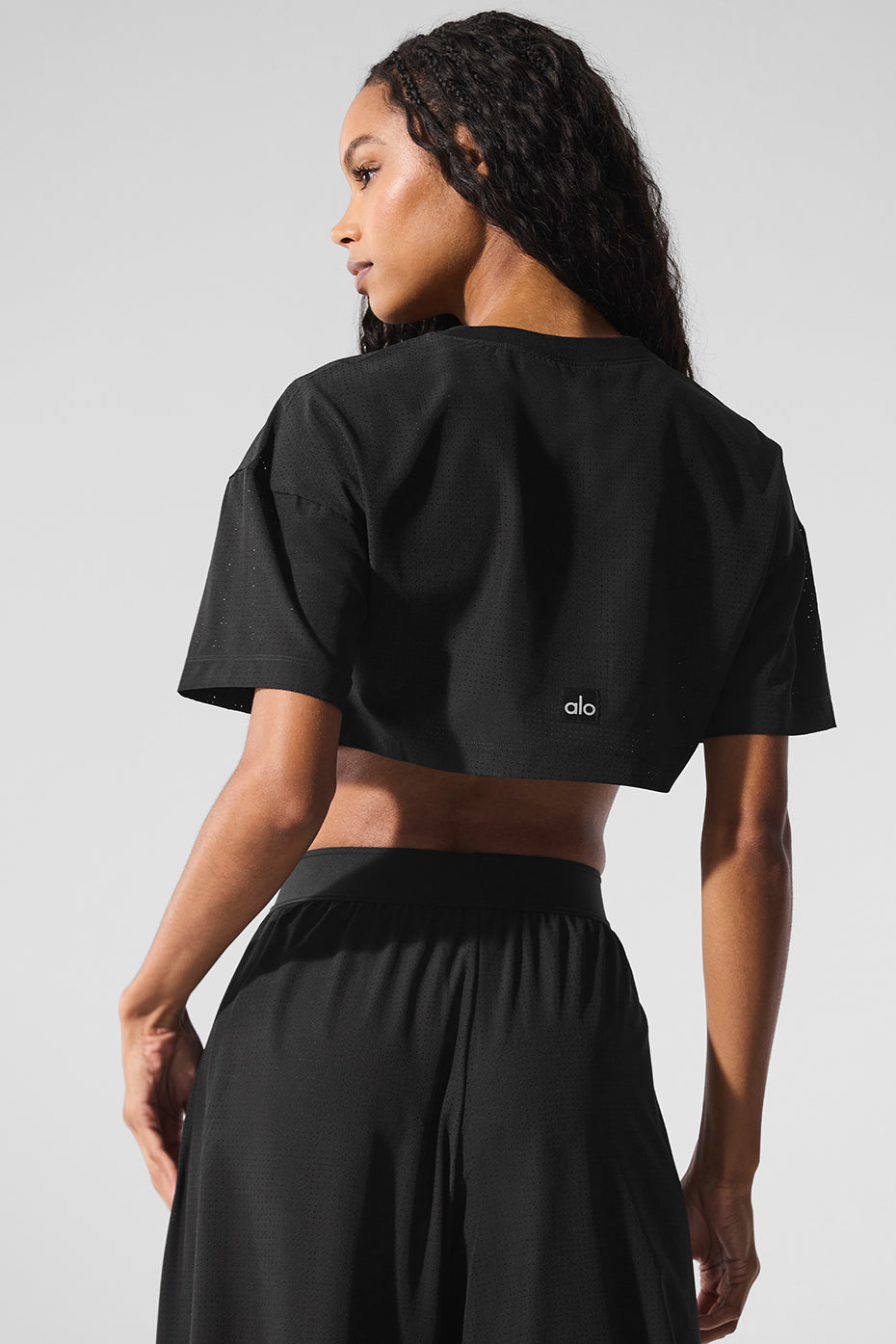 Model wearing black Mesh Cropped Mirage Tee showcasing its cropped fit and longer sleeves, perfect for sunny days.