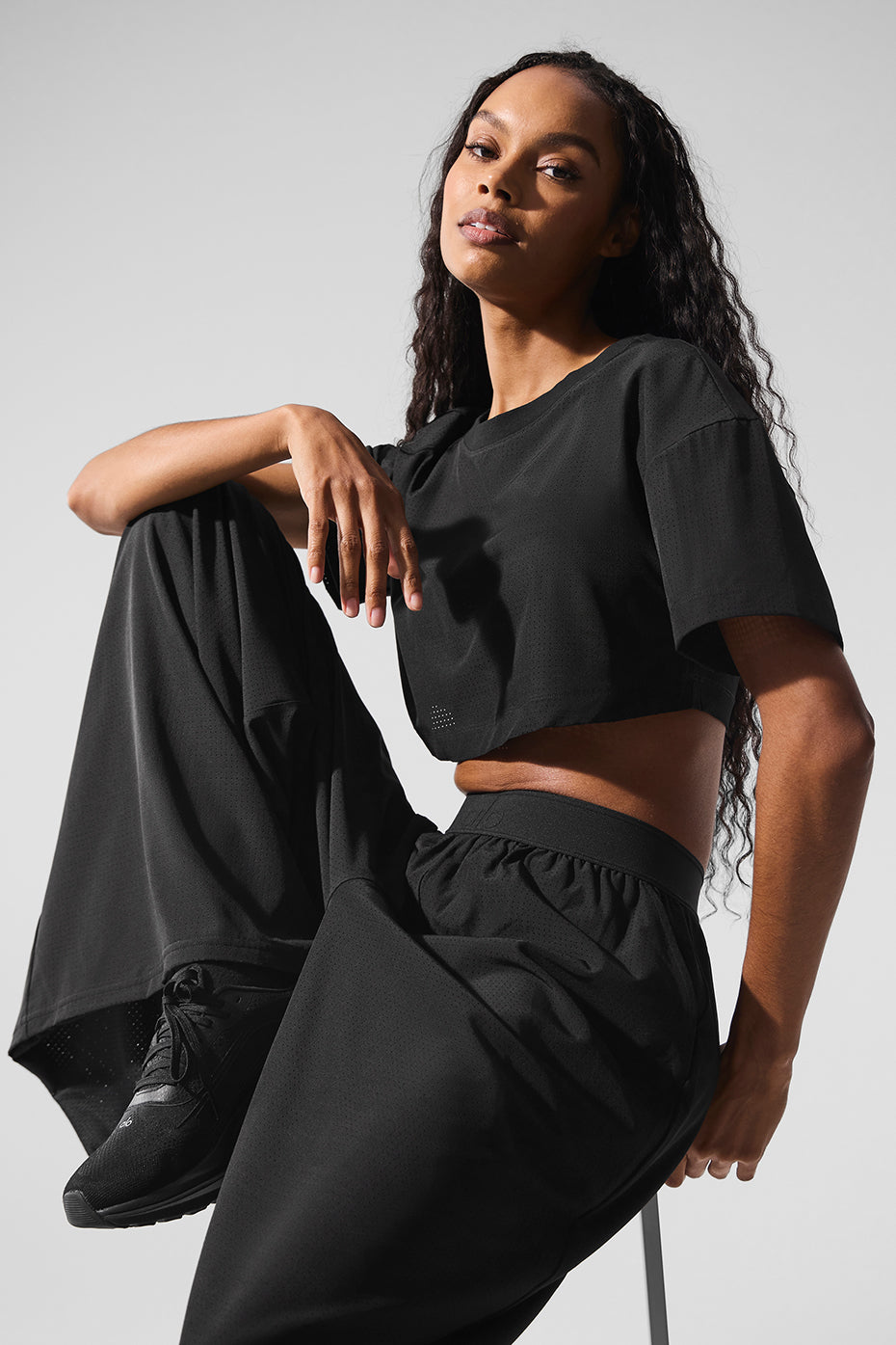 Model wearing a Mesh Cropped Mirage Tee with relaxed fit and longer sleeves, paired with chic black pants.