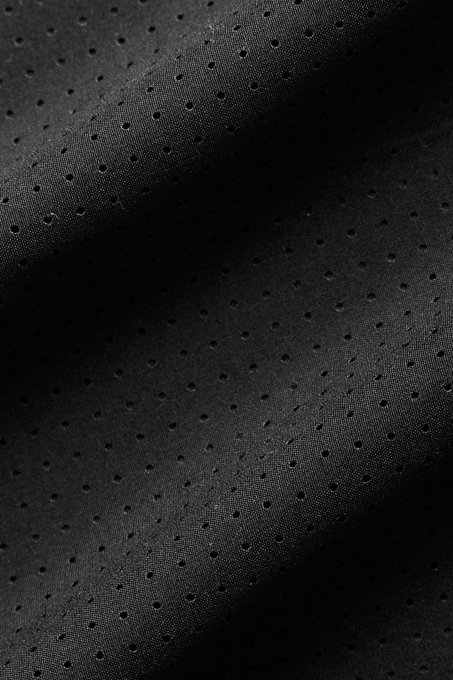 Close-up of lightweight black perforated fabric, ideal for breathable and stylish apparel like the Mesh Cropped Mirage Tee.