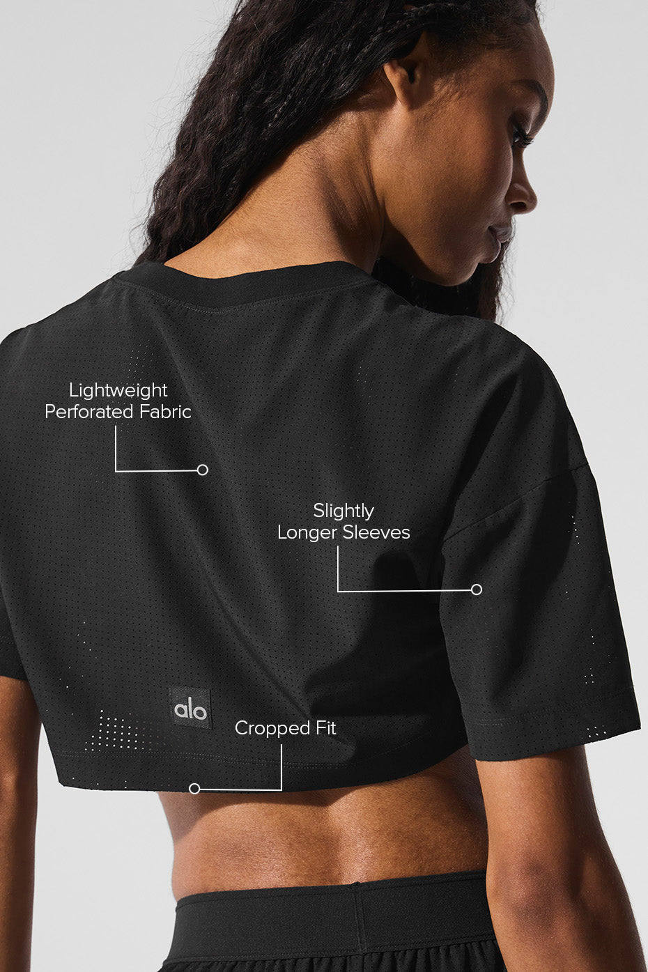 Back view of a model wearing the Mesh Cropped Mirage Tee showcasing lightweight perforated fabric and slightly longer sleeves.
