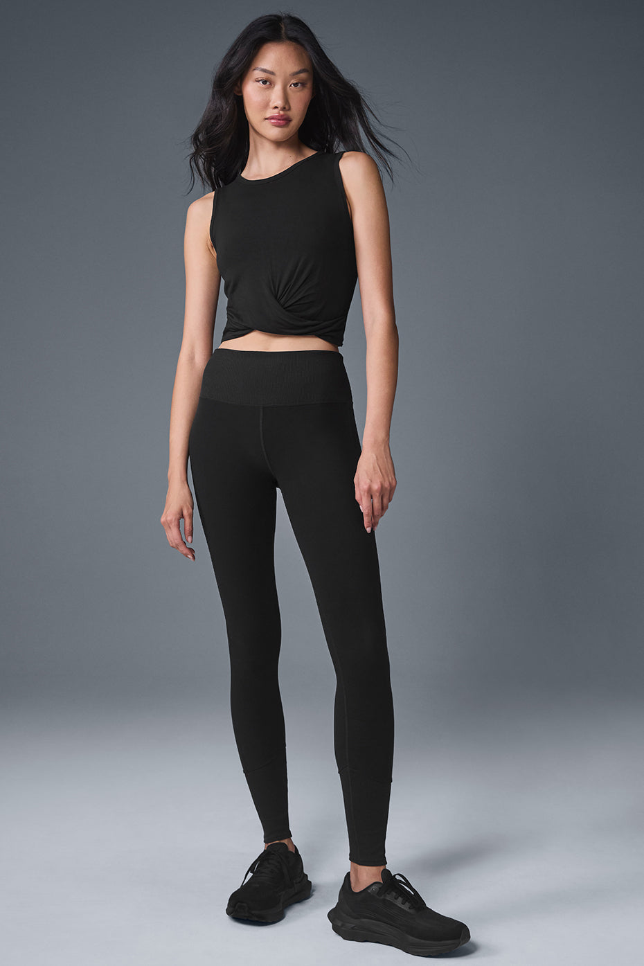 Model wearing a fitted black Cover Tank top with front wrap detail and black leggings, showcasing a stylish athleisure look.