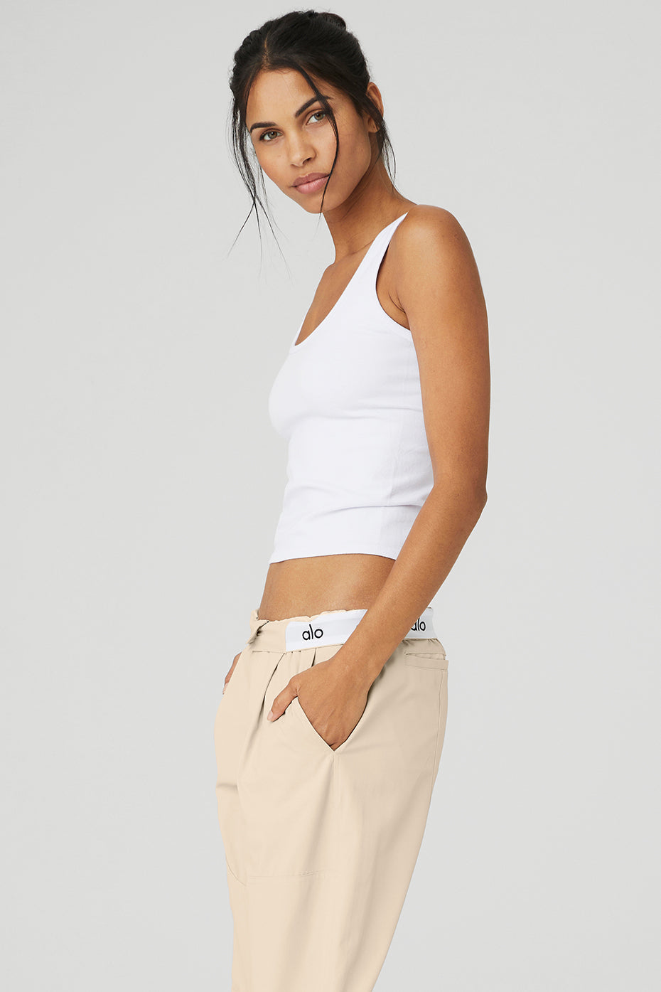 Model wearing a seamless, feather-light white tank top with a fitted silhouette and deep scoop neck, paired with beige pants.