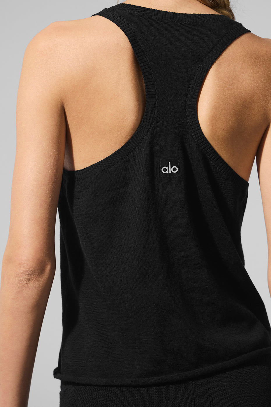 Back view of a black lightweight knit sweater tank with a relaxed fit and branded logo for a stylish look.