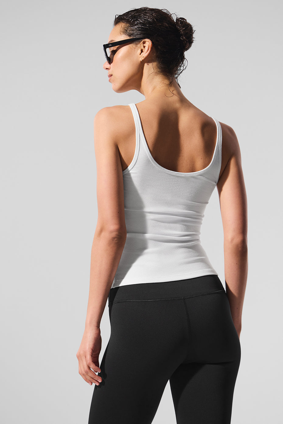 Model wearing white Ribbed Prosper Tank top with black leggings, showcasing a body-skimming fit and minimalistic design.