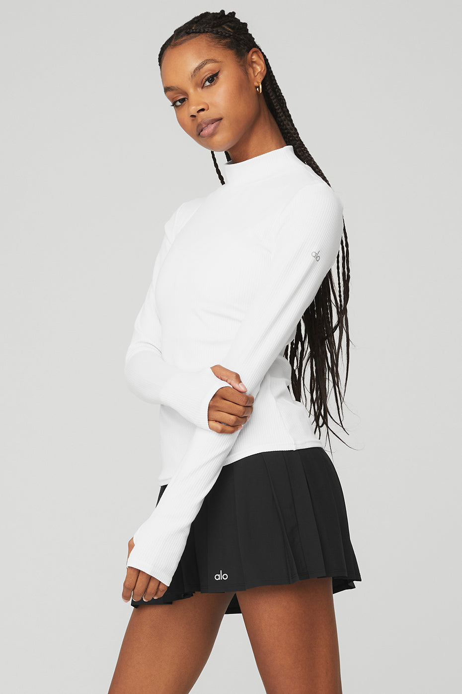 Model wearing Wellness Rib Mock Neck Long Sleeve top in white, featuring ribbed fabric and full-length sleeves, paired with a black pleated skirt.