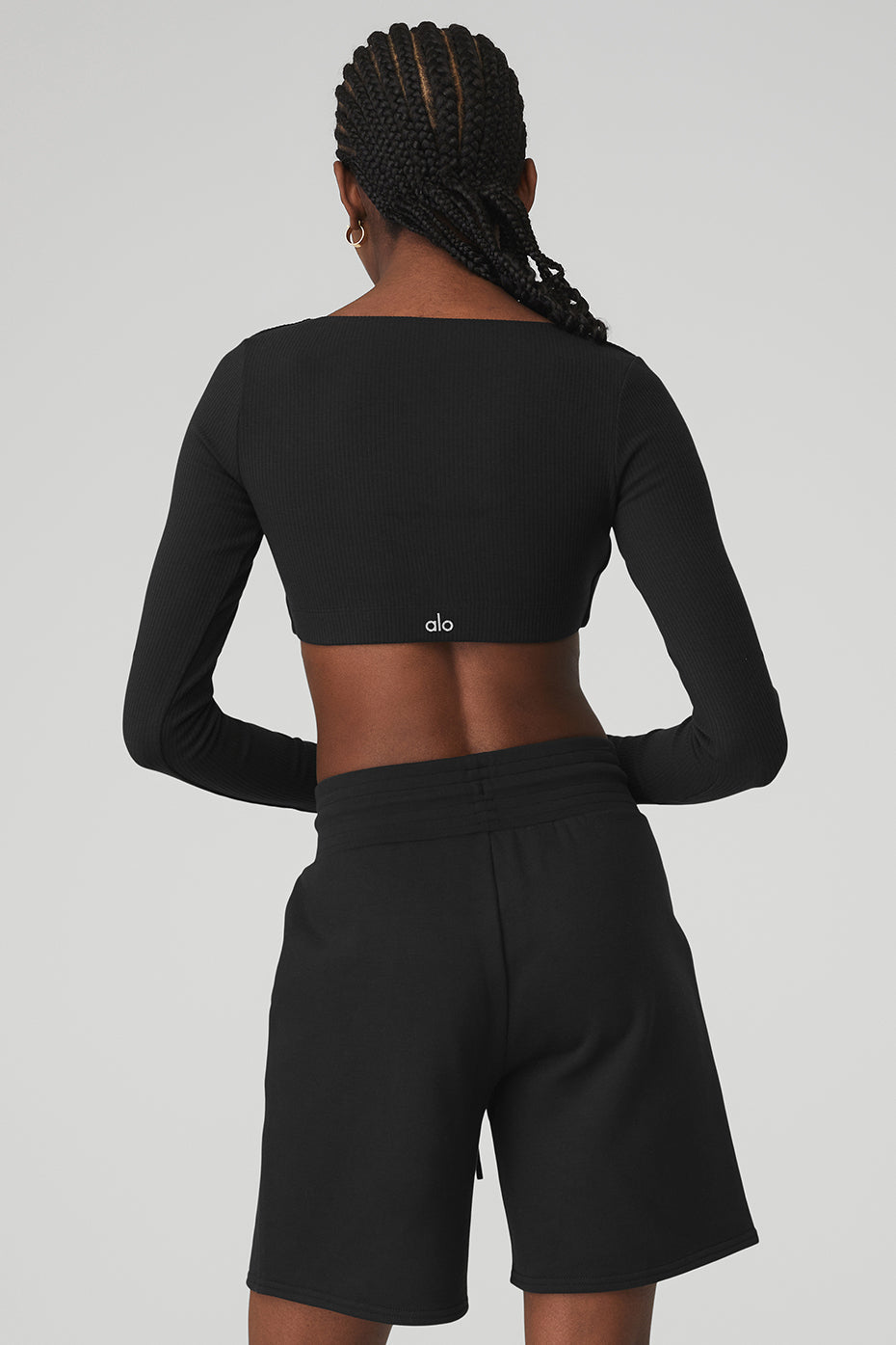 Back view of a woman wearing a black ribbed long sleeve cropped bra and matching shorts, showcasing light support and stylish comfort.