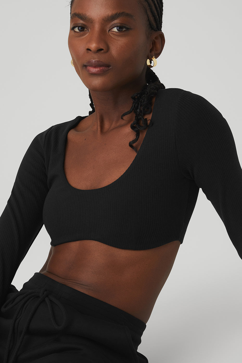 Model wearing a ribbed defined long sleeve cropped bra top in black with a scoop neck and light support.