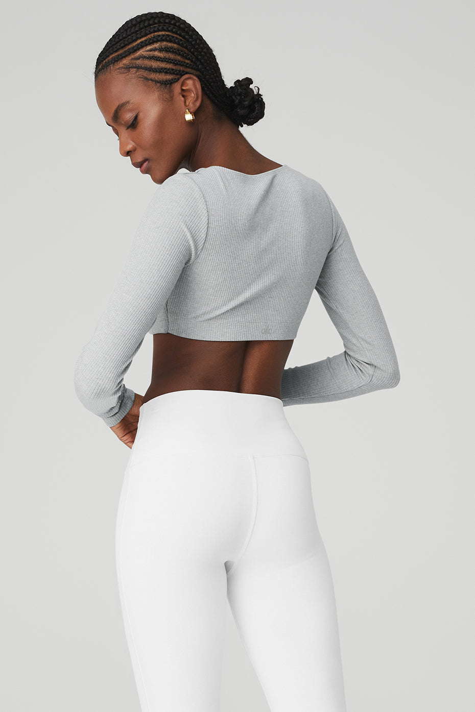 Back view of woman wearing a ribbed defined long sleeve bra with scoop neck and white flared leggings.