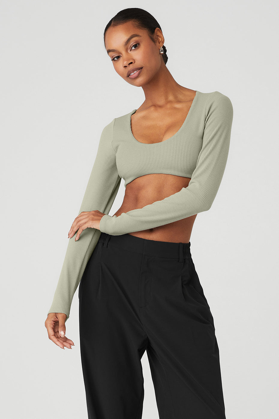 Model wearing a ribbed defined long sleeve bra in green, paired with black pants, showcasing its comfy fit and scoop neck design.