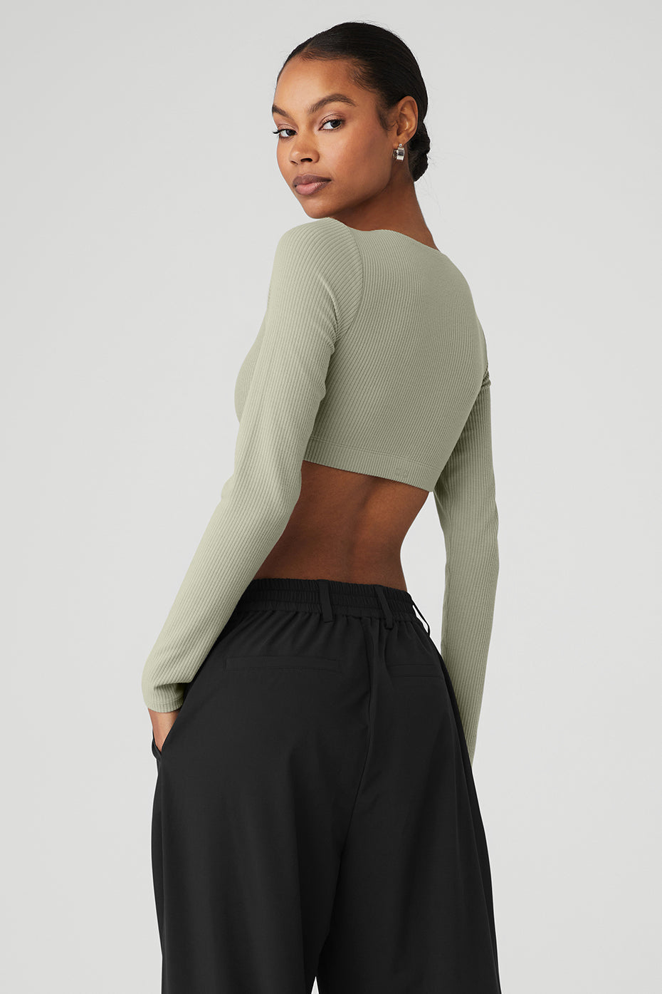 Back view of a model wearing a ribbed defined long sleeve bra in soft green with cropped styling and fitted design.