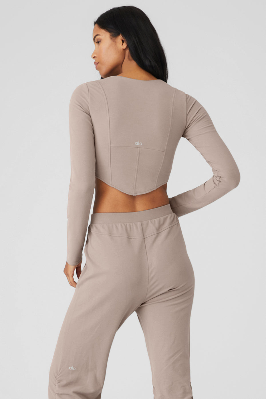 Back view of woman in ALO Softsculpt Long Sleeve crop top with corset panels and matching pants.