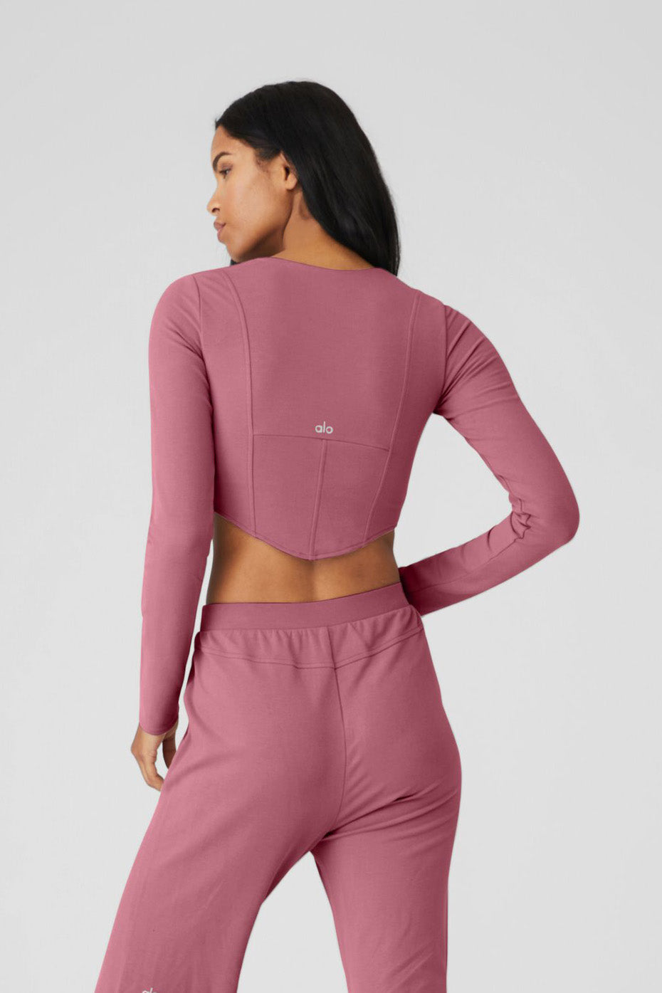 Back view of ALO Softsculpt Long Sleeve crop top in pink, featuring a corset-style design and long sleeves.