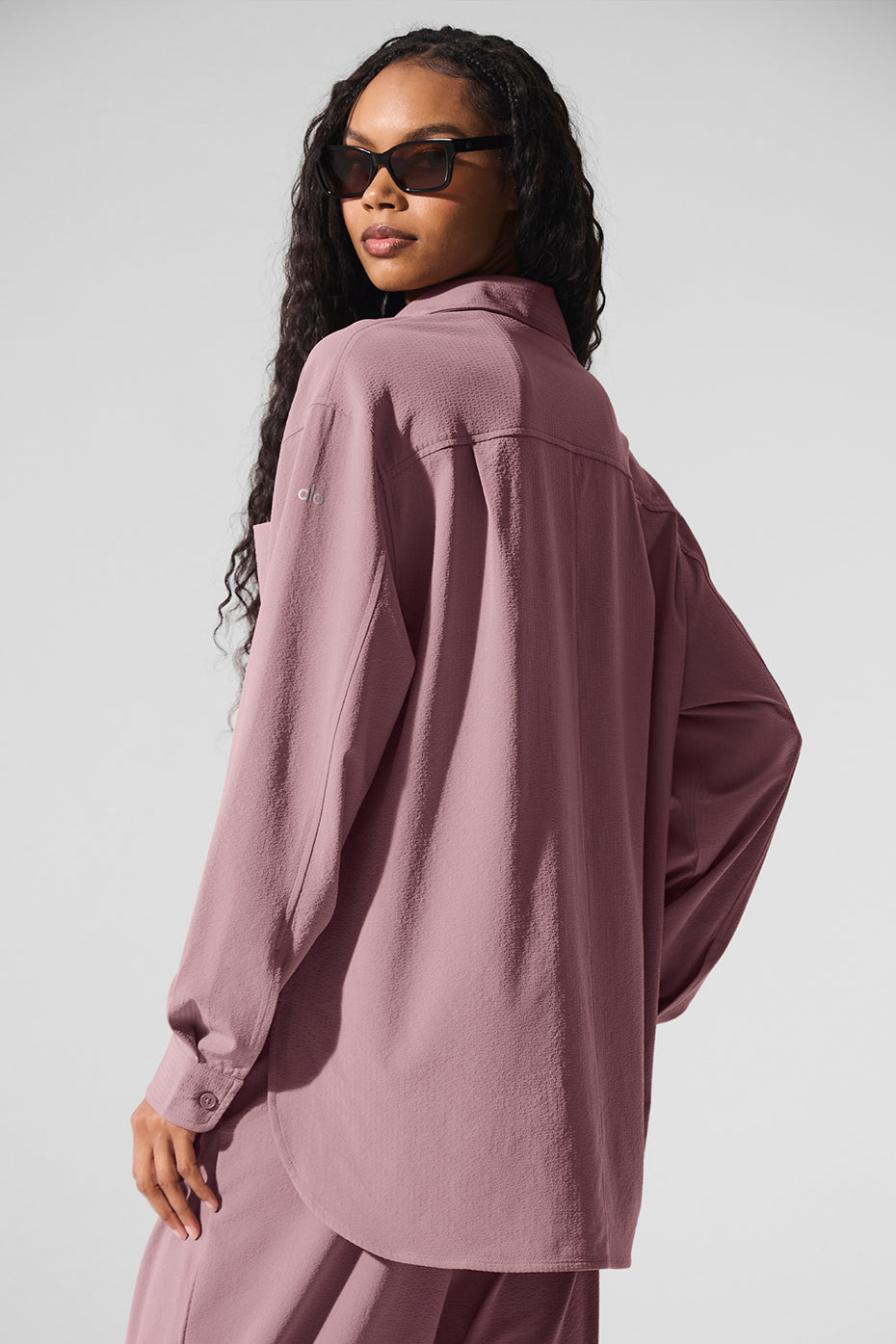 Woman wearing a lightweight Dreamscape Button Down Long Sleeve in light pink, showcasing its oversized fit and crinkle woven fabric.