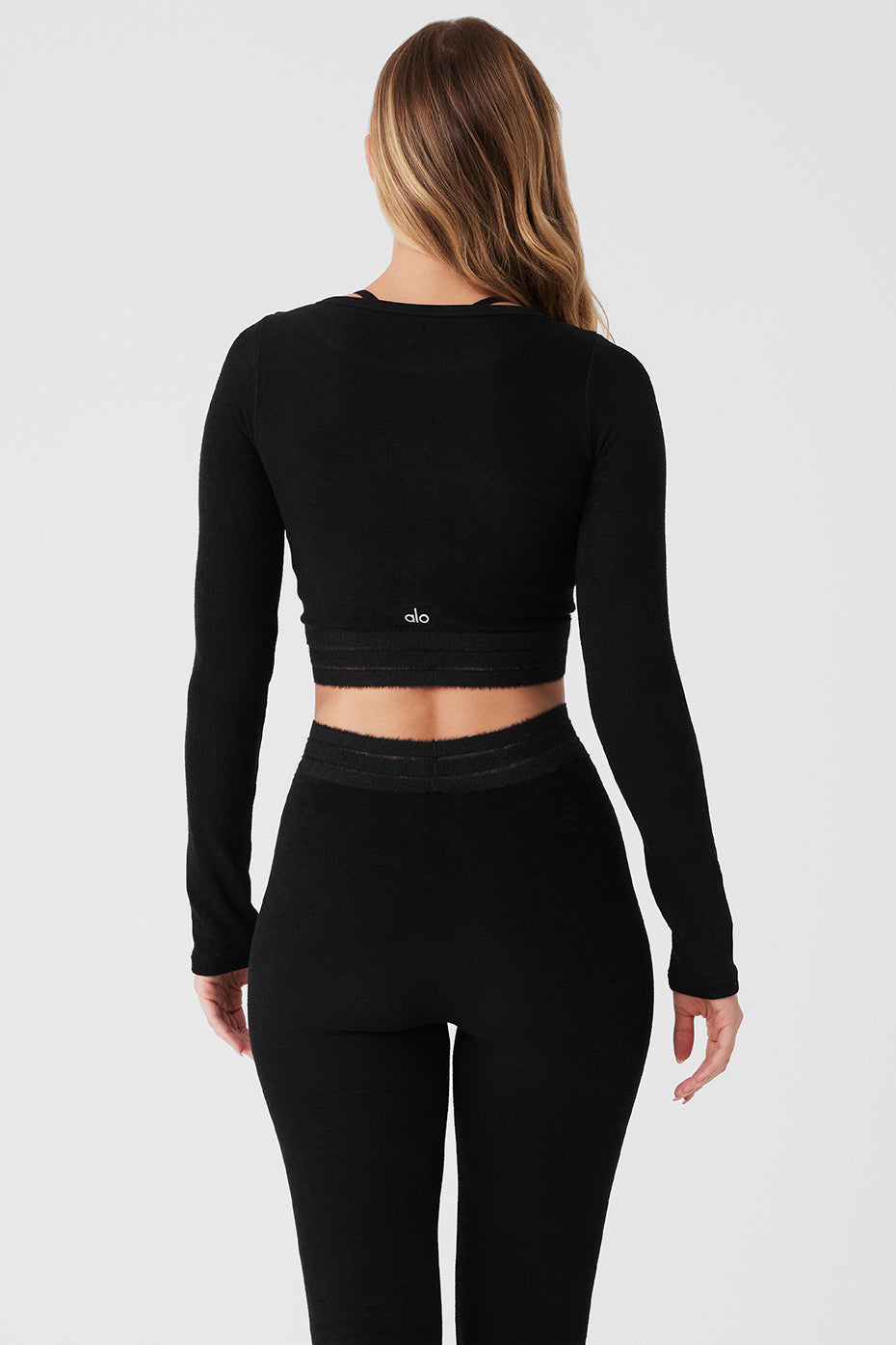Back view of woman in black Seamless Luxe Terry Cuddle Coverup and matching leggings, showcasing its crop design and luxe fabric.
