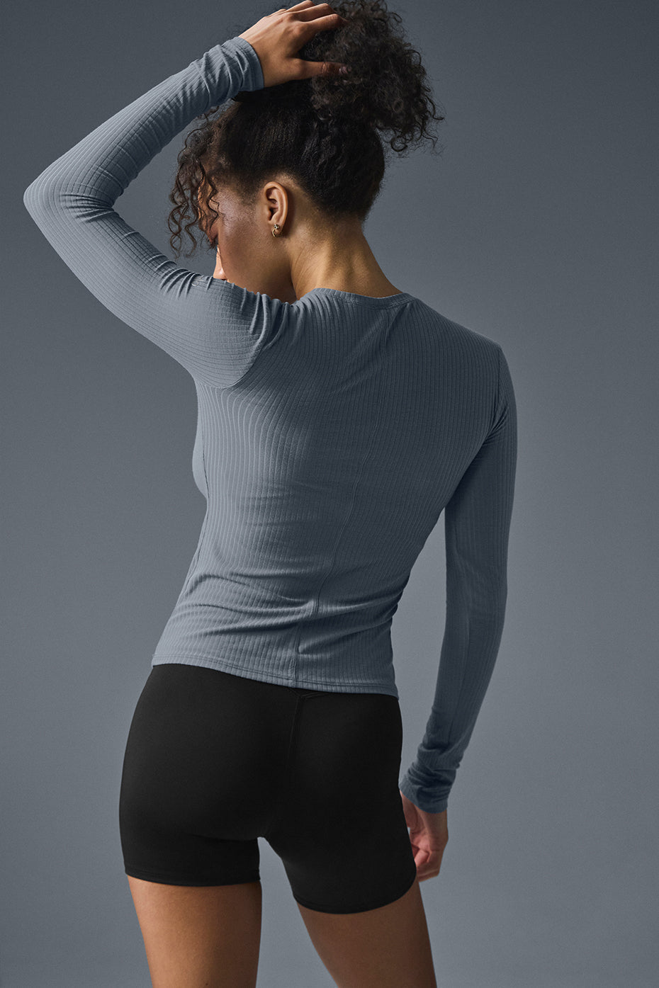 Back view of a woman wearing the Ribbed Sea Coast Long Sleeve shirt paired with black shorts.