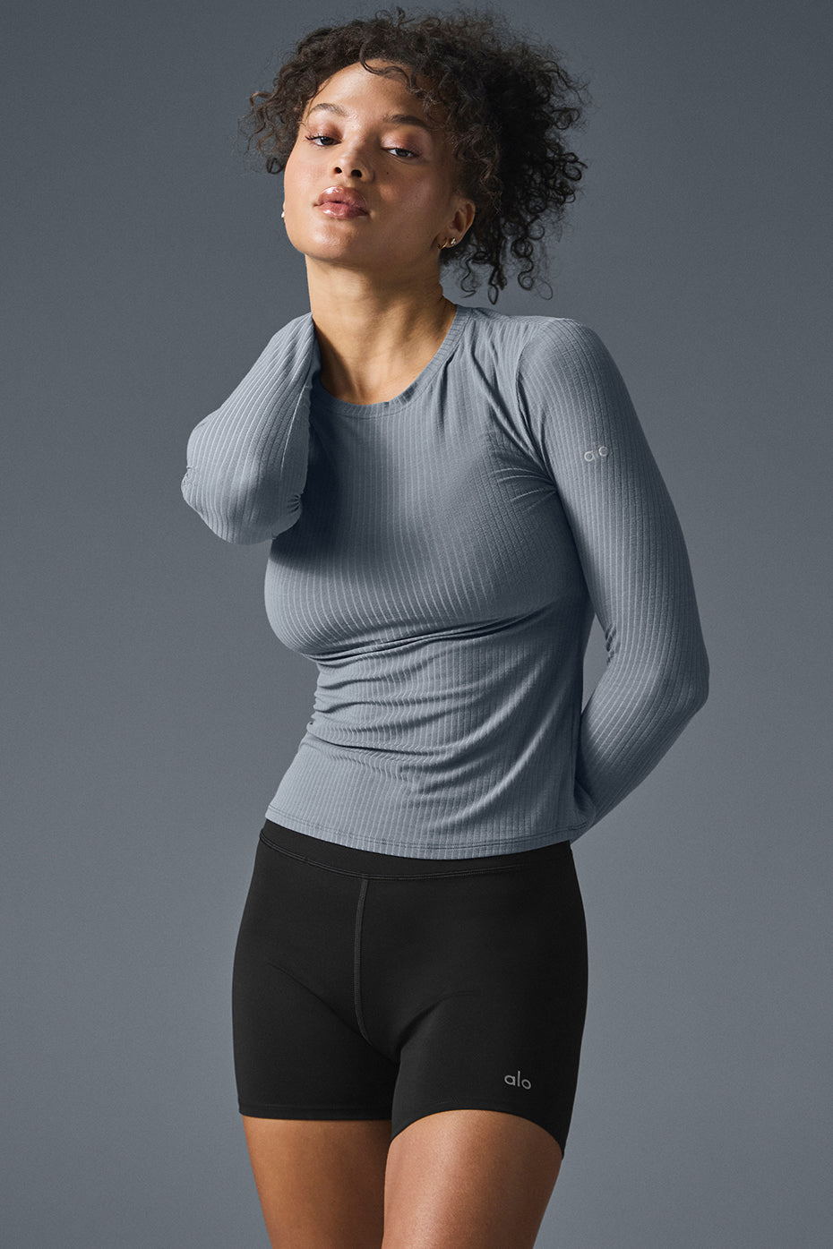 Model wearing a ribbed long sleeve shirt in sea coast color, paired with black shorts, showcasing soft and stretchy fabric.