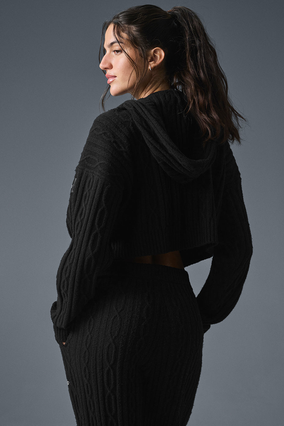 Model wearing a black cable knit winter hoodie with a cropped hem and relaxed fit, showcasing cozy winter vibe.