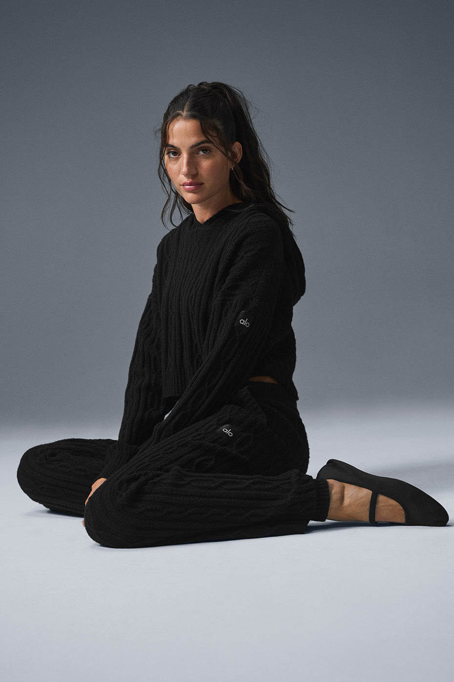 Model wearing a black cable knit Winter Bliss Hoodie with matching pants, showcasing cozy winter fashion.
