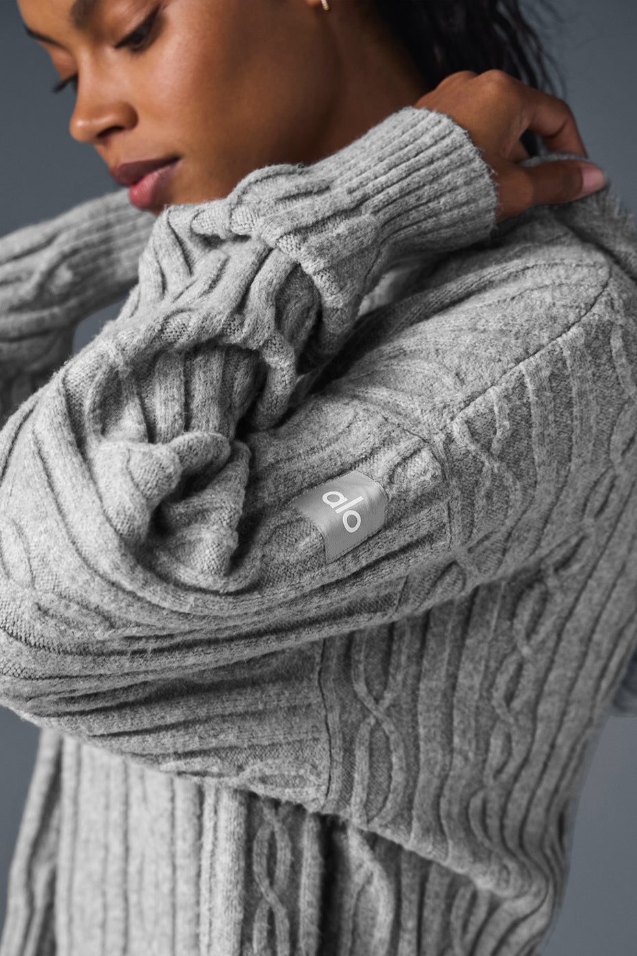 Close-up of a woman wearing a gray cable knit hoodie with relaxed fit and branded sleeve detail.