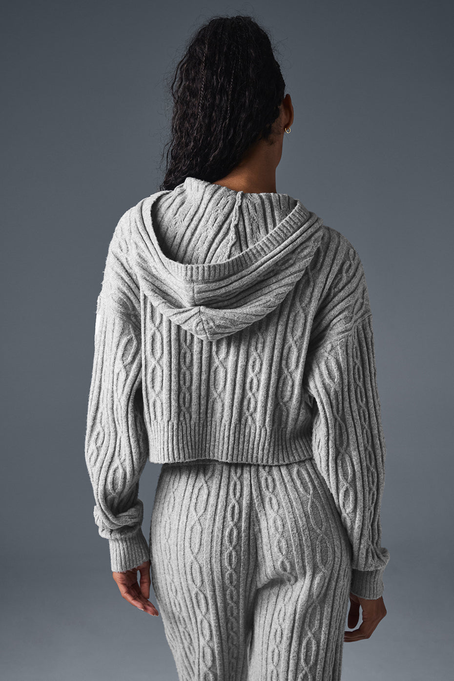 Back view of a woman in a gray cable knit winter bliss hoodie showcasing its relaxed fit and cropped design.