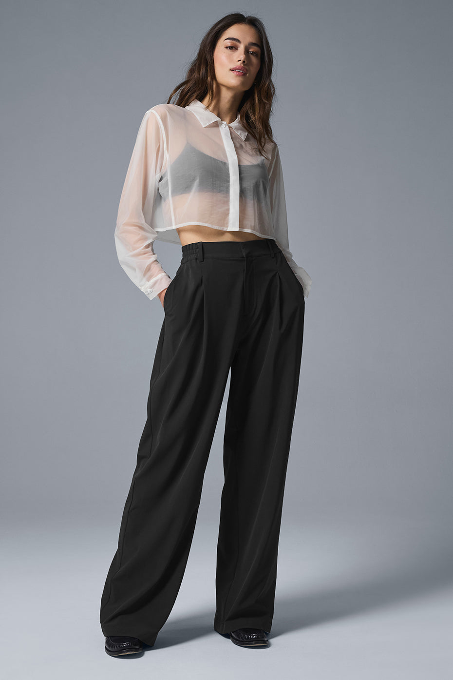 Model wearing sheer cropped button-up shirt with trousers showcasing chic, loose fit and stylish details.