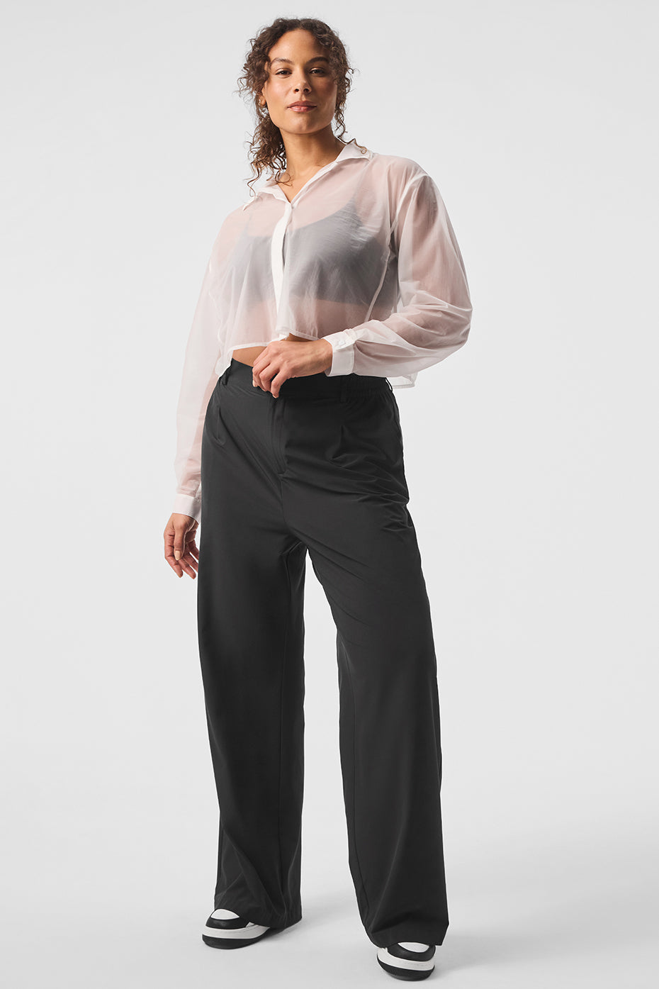 Model wearing a sheer cropped button-up shirt with trousers, showcasing chic style and versatility.