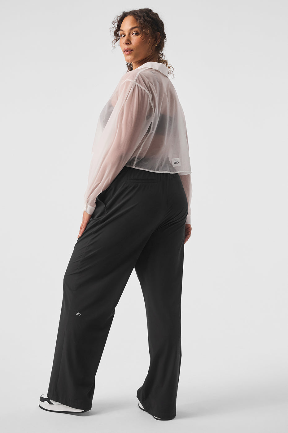 Model wearing a sheer cropped button-up blouse with cuffs and loose black trousers, showcasing a chic style.