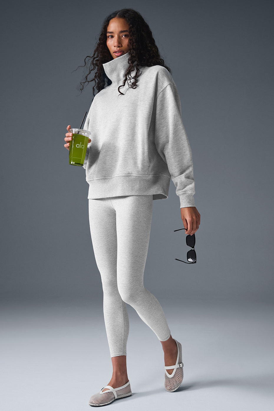Model wearing a Hazy Mock Neck Pullover with leggings and sipping green juice, showcasing a cozy oversized fit.