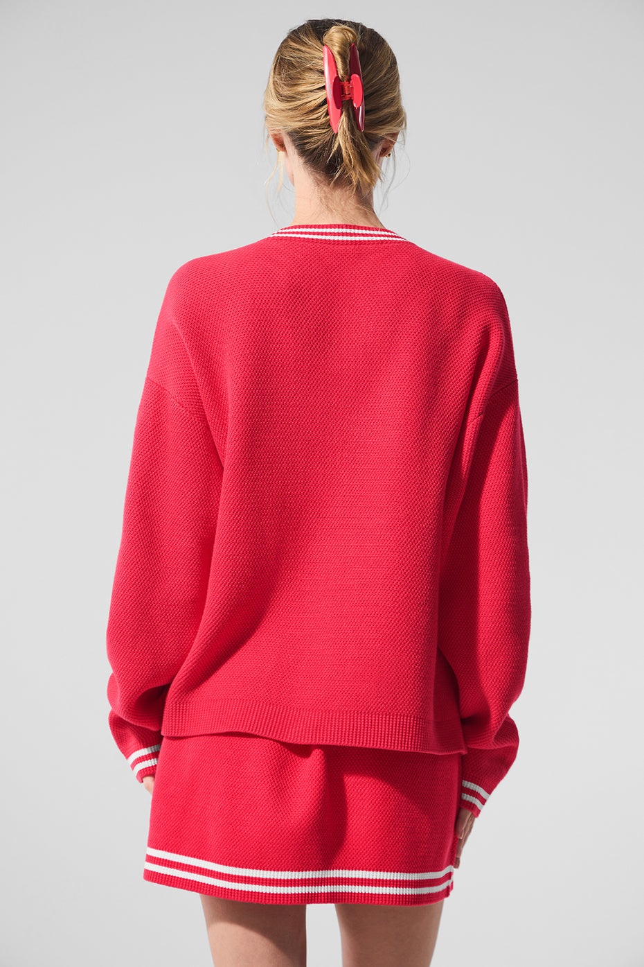 Back view of a female wearing a red Tennis Club sweater knit cardigan with striped trim and relaxed fit.