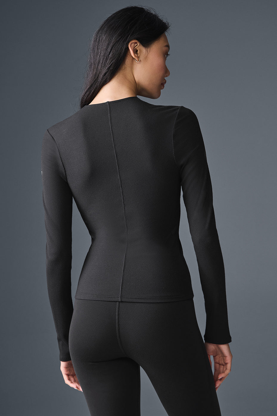 Back view of a woman wearing a ribbed black long sleeve top with a close-to-body fit, ideal for layering.