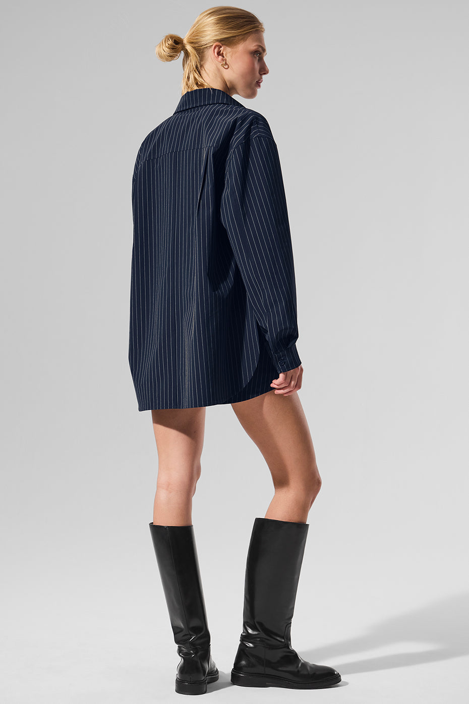 Model wearing a pinstripe button down long sleeve shirt styled with knee-high black boots from the back.
