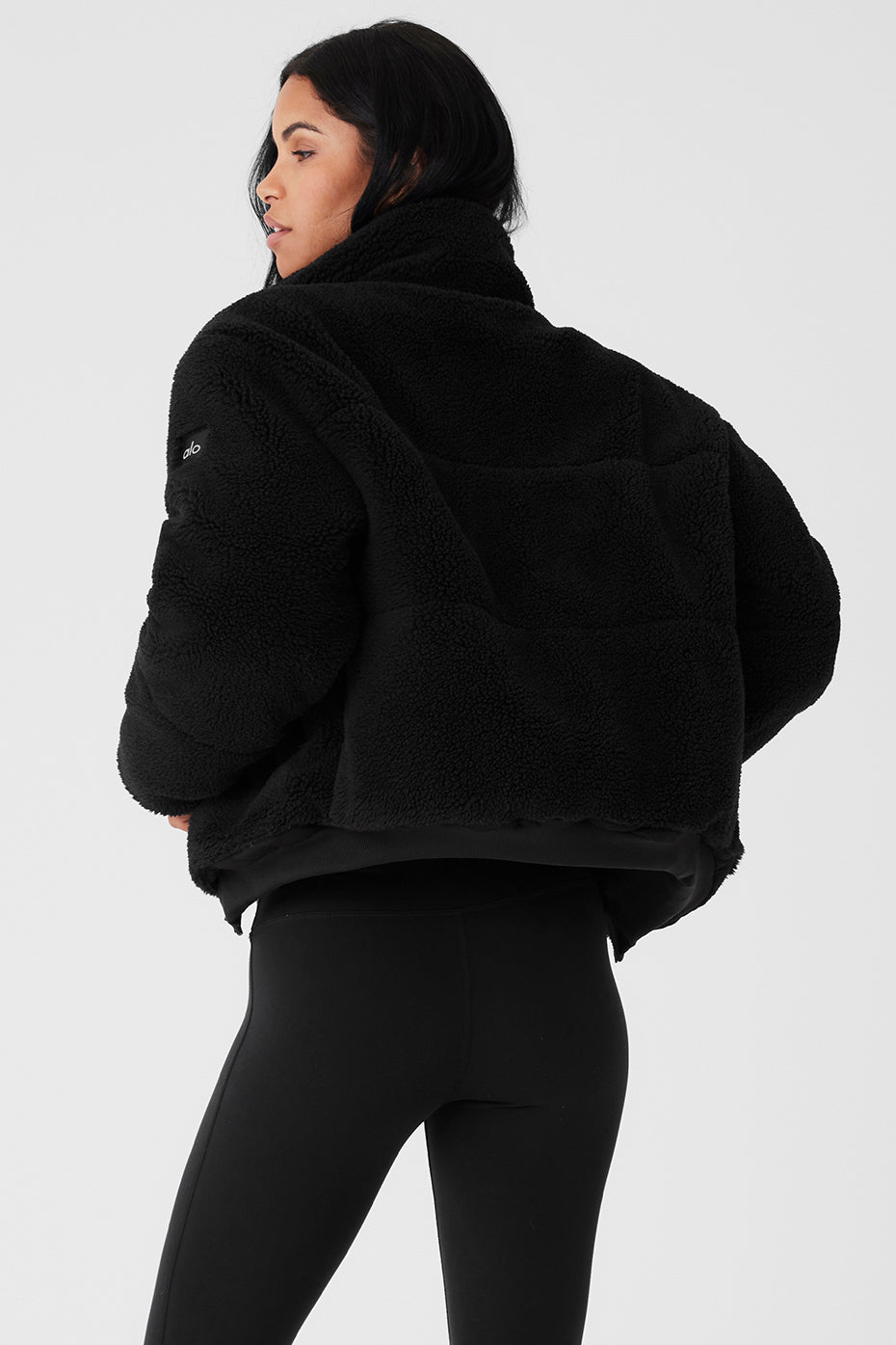 Back view of a woman wearing a black Sherpa Snow Angel puffer with a tall collar and cozy fit.