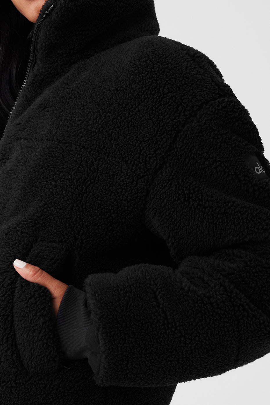Close-up of a plush black sherpa puffer jacket featuring a tall collar and deep zippered pockets.