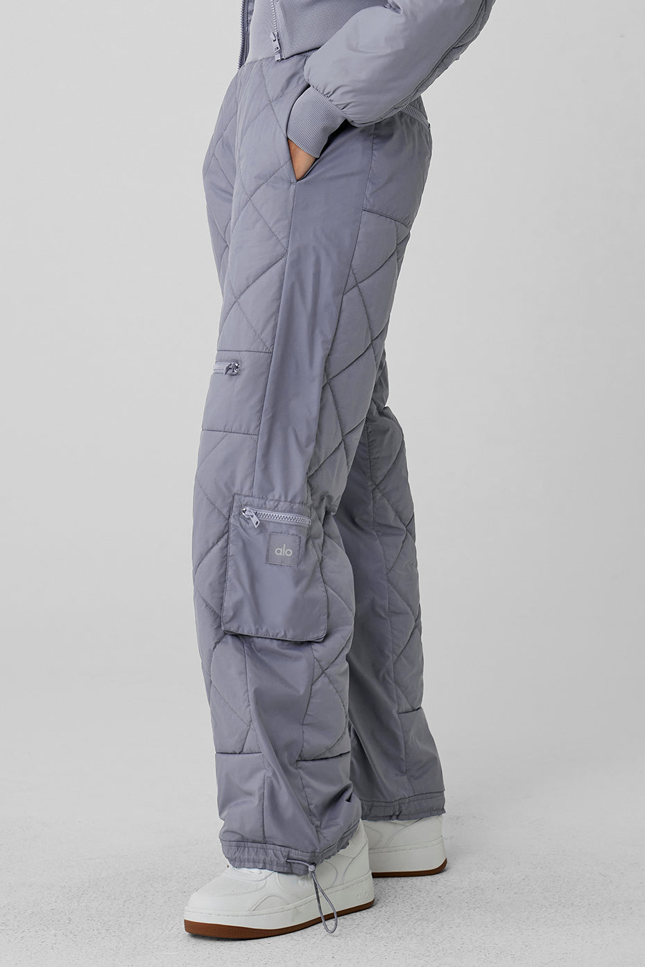 High-waist Snowrider puffer pant in gray, featuring quilted finish, wide ribbed waistband, and multiple zippered pockets.