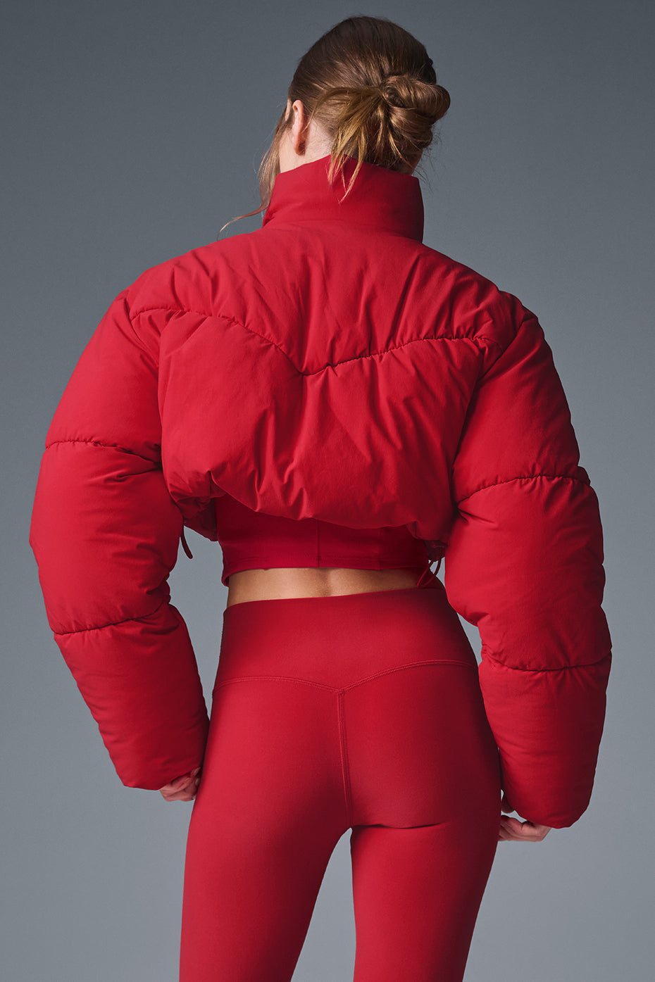 Back view of a model wearing a red Main Act Corset Puffer jacket with a cropped silhouette and corset hem.