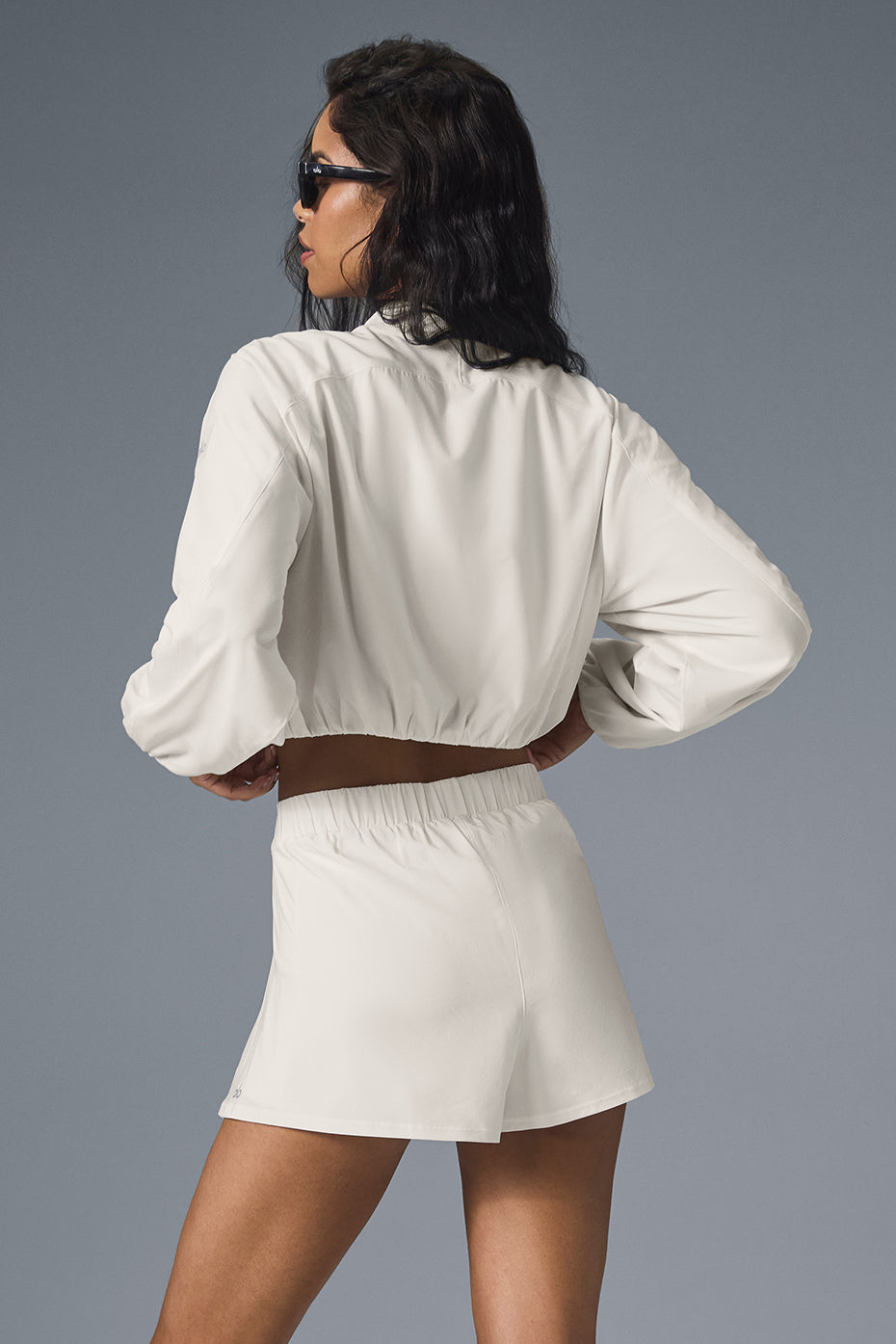 Back view of a model wearing a cropped Tiebreaker Jacket with matching shorts, showcasing a stylish athletic look.