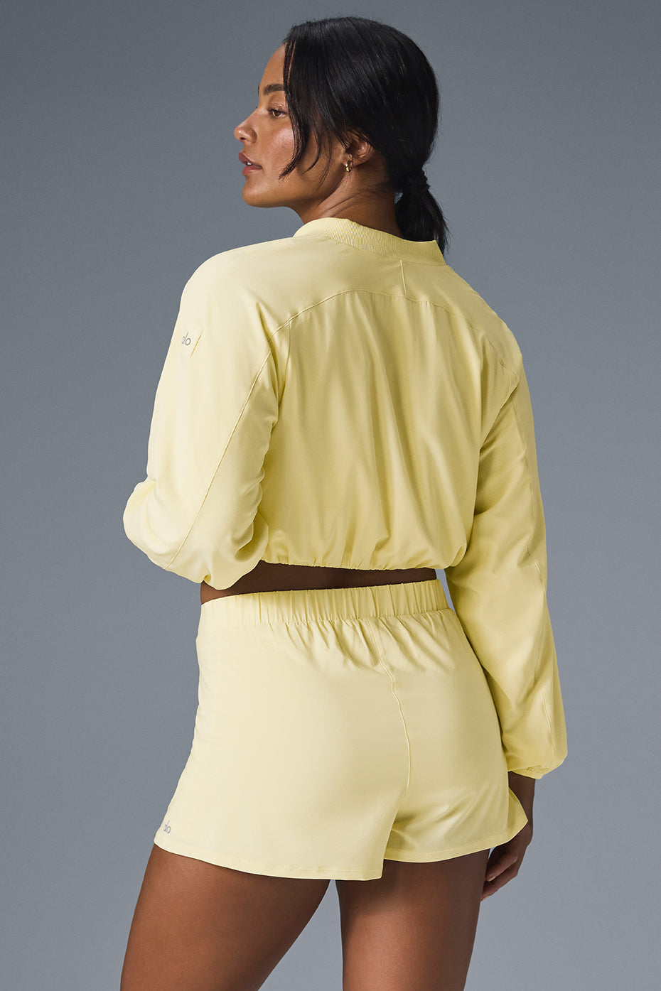Model wearing a Tiebreaker Jacket in yellow, showcasing a cropped hem and matching Tiebreaker Short for activewear style.