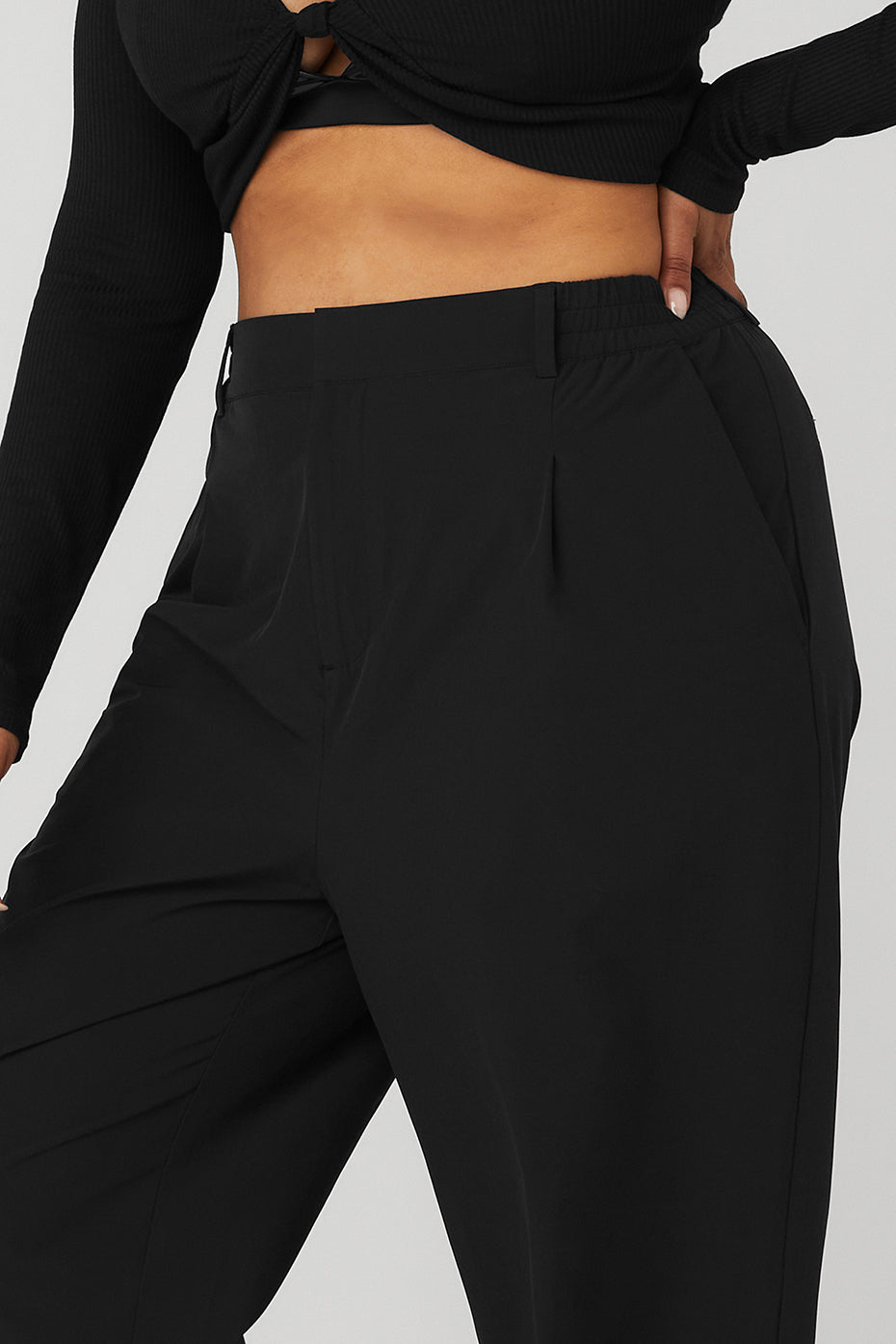 Close-up of high-waist pursuit trousers featuring elastic waistband, pleats, and relaxed wide-leg fit in black.