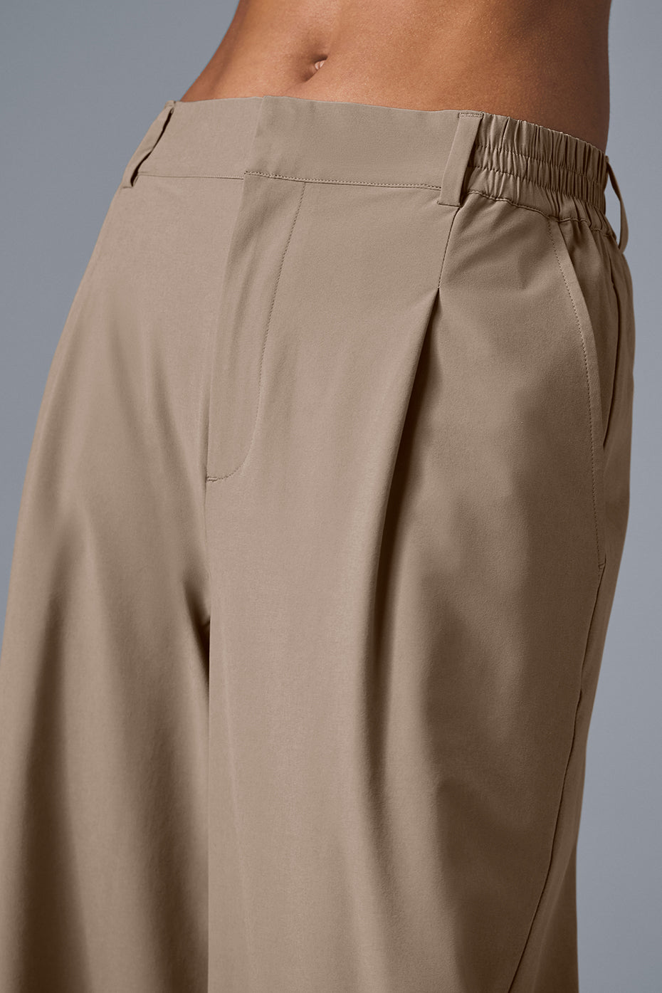 High-waist pursuit trousers featuring a high-rise waistband, pleats, and relaxed wide-leg fit in a sleek light fabric.