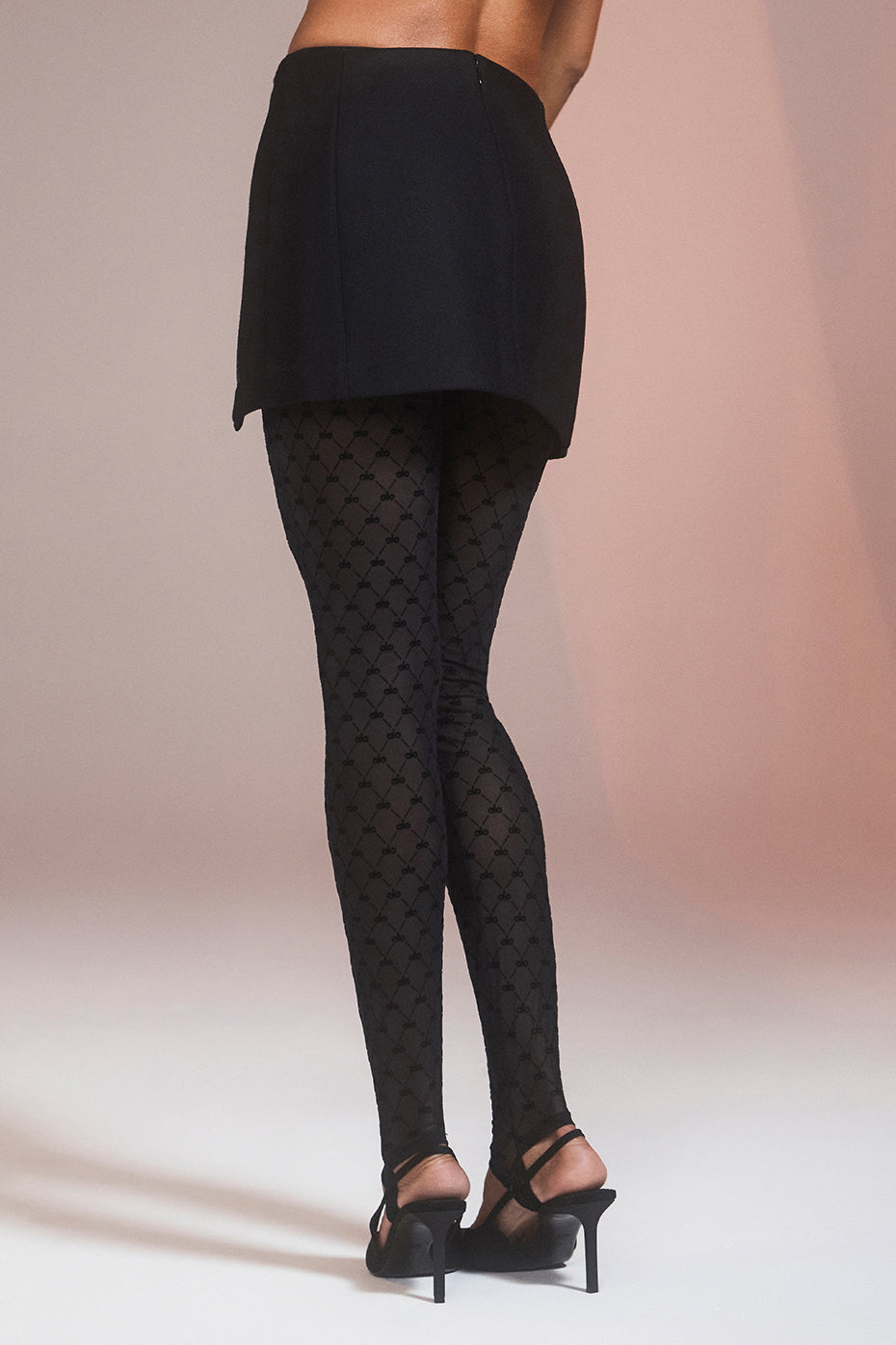 Back view of a model wearing a Winter Wool Vendome Mini Skirt with patterned tights and heels, showcasing a sleek A-line silhouette.