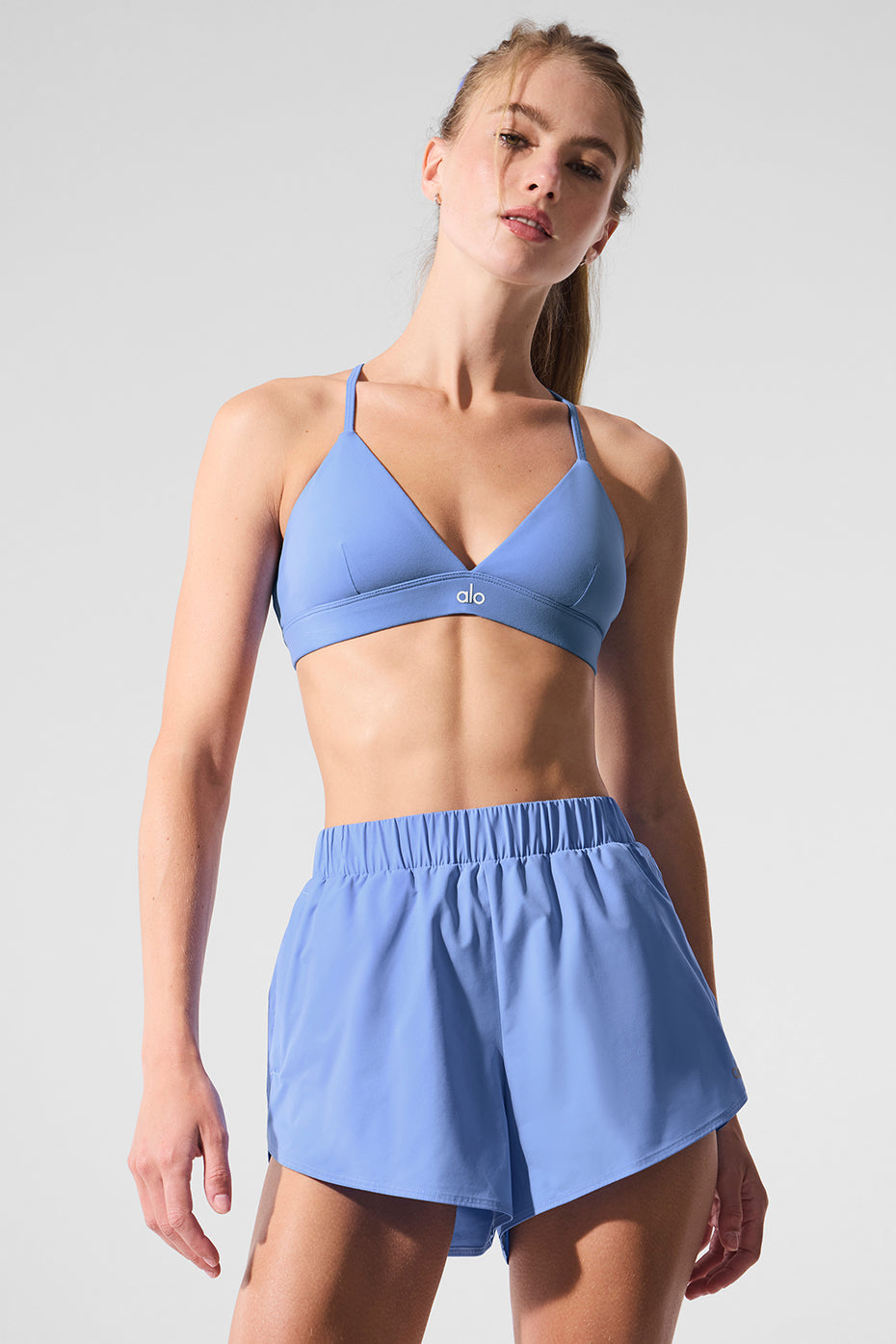 Model wearing Playmaker Dolphin Shorts with a stylish blue sports bra, showcasing sporty and chic activewear.