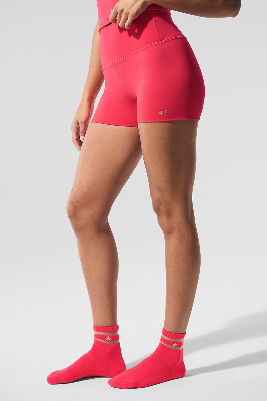 Model wearing 3" ALO Softsculpt High-Waist Precision Short in pink with matching socks showcasing a seamless design.